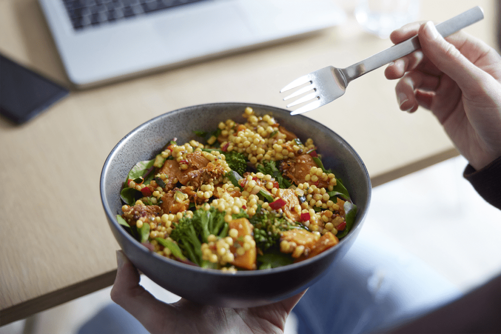 photo of someone holding a bowl of grains and vegetables in one hand, and a fork in the other
